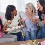 Friends drinking white wine and sharing cupcakes at party at home on couch