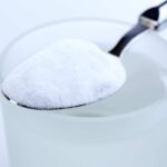 Spoon of baking soda over glass of water, isolated on white