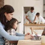 Busy Family Home With Mother Working As Father Prepares Meal