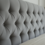Close-up detail of a vintage capitone tufted velvet headboard in soft grey pearl color, showing the