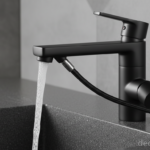 Close-up of a matte black monomando kitchen faucet with pull-out spray head, water flowing into a co