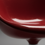 Extreme close-up detail of the curved glossy thermoplastic surface of a designer armchair in red, sh