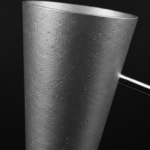 Extreme macro close-up of a brushed aluminum cone-shaped magazine holder cup attached to a slim polished steel rod, showin…
