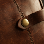 Macro close-up detail of cognac brown aged leather texture with visible hand-stitched edge and a pol