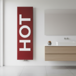 Modern minimalist bathroom with a bold red Italian designer radiator featuring the word ‘HOT’ embossed in large uppercase …