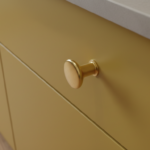 Close-up detail of a mustard yellow matte lacquered kitchen cabinet door with round brass pull handl