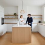 Stylish modern kitchen with cork flooring, white cabinets, and wooden accents, a couple standing and