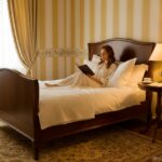 A cozy Biedermeier style bedroom with a wooden bed frame in walnut, white linens, a small round side