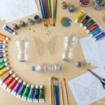 Crafting materials laid out on a wooden table for making recycled butterflies: plastic bottles, colo