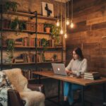 Woman working on laptop in a cozy rustic industrial office with stone walls, wooden shelves with boo
