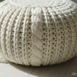 Close-up detail of a chunky knitted wool pouf ottoman in cream white color, showing the thick yarn t